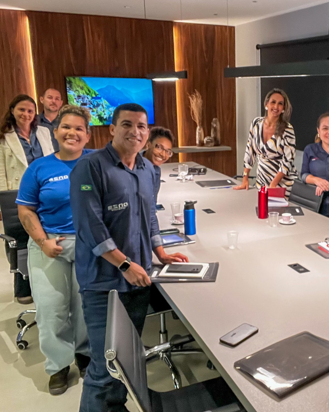 Grupo em pé em sala de reunião com painel de madeira ao fundo